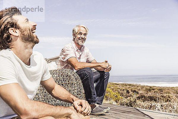 Vater und erwachsener Sohn hängen zusammen auf einer Terrasse am Meer herum und amüsieren sich