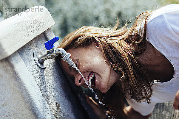 Glückliches Teenager-Mädchen trinkt Wasser aus einem Brunnen