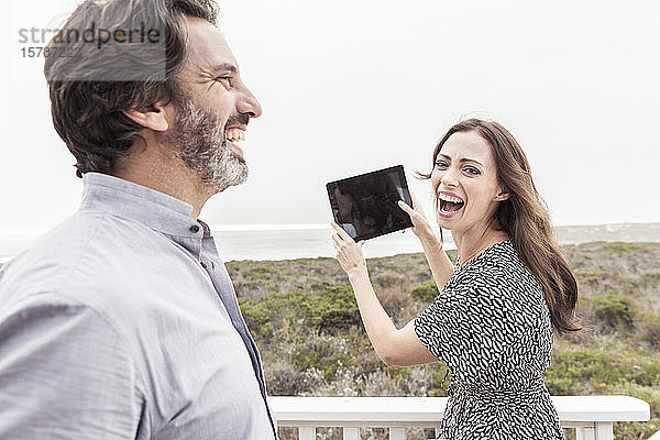 Glücklicher Mann mit Frau hält Tablette an der Küste