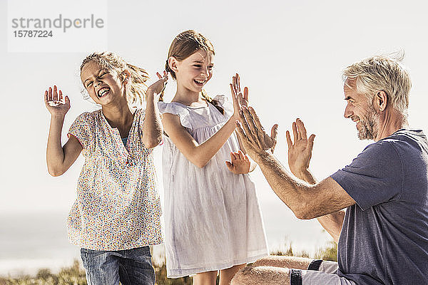 Zwei glückliche Mädchen klatschen mit ihrem Großvater in die Hände
