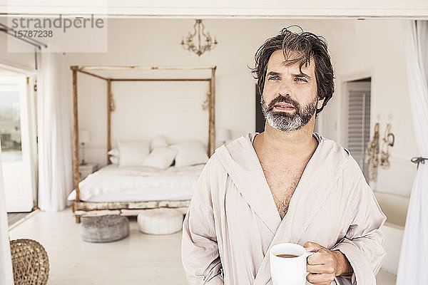 Mann im Bademantel mit einer Tasse Kaffee im Schlafzimmer