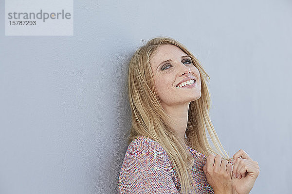 Porträt einer lächelnden blonden jungen Frau  die einen an die Wand gelehnten Strickpullover trägt