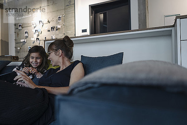 Glückliche Frau und Mädchen sitzen im Büro auf der Couch und benutzen ein Smartphone