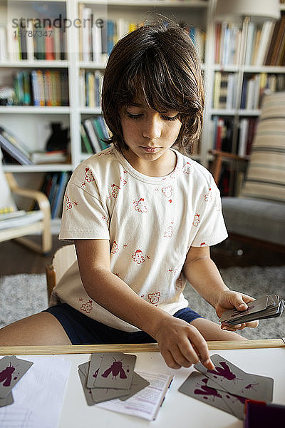 Porträt eines Jungen  der zu Hause mit Spielkarten am Tisch sitzt