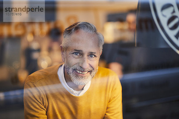 Porträt eines lächelnden reifen Mannes hinter Glasscheibe in einem Cafe