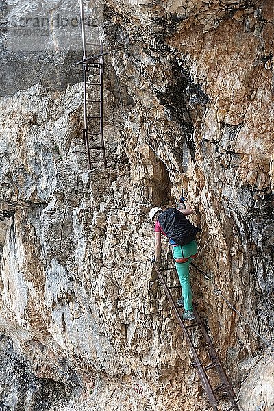 Junge Frau  Wanderer steigt eine Leiter hinunter  während sie in einem Klettersteig klettert  der an einem Stahlseil gesichert ist  Klettersteig Francesco Berti  Sorapiss Rundweg  Dolomiten  Belluno  Italien  Europa