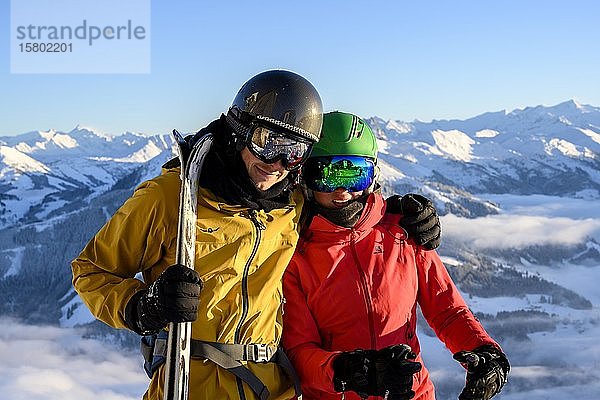 Zwei Skifahrer mit Skihelmen und Skiern stehen vor einem Bergpanorama  Paar  Blick in die Kamera  SkiWelt Wilder Kaiser  Brixen im Thale  Tirol  Österreich  Europa