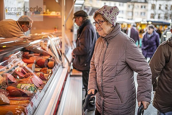 Seniorin schaut sich die Wurstwaren eines Metzgers auf dem Wochenmarkt an  Köln  Nordrhein-Westfalen  Deutschland  Europa