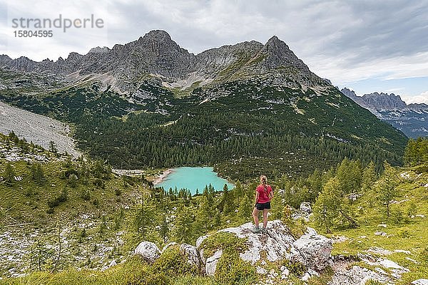 Junge Frau  Wanderer steht auf Felsen und schaut auf den türkisgrünen Sorapiss-See und die Berglandschaft  Dolomiten  Belluno  Italien  Europa