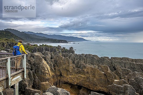 Junger Mann auf Aussichtsplattform mit Blick auf Küstenlandschaft mit Sandsteinfelsen  Pancake Rocks  Paparoa National Park  Punakaiki  Westküste  Südinsel  Neuseeland  Ozeanien