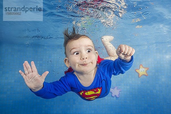 Kleiner Junge im Superman-Kostüm taucht im Schwimmbad unter Wasser  Vorderansicht  Ukraine  Europa