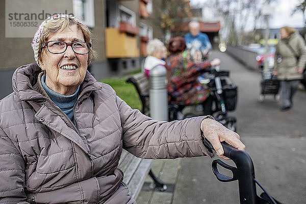 Seniorin sitzt auf einer Bank vor einer Seniorenwohnanlage  Köln  Nordrhein-Westfalen  Deutschland  Europa