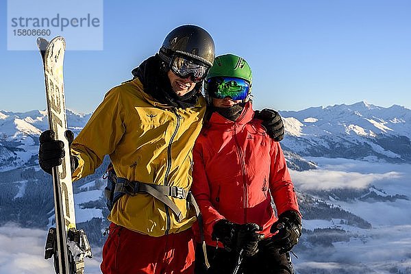 Zwei Skifahrer mit Skihelmen und Skiern stehen vor einem Bergpanorama  Paar  Blick in die Kamera  SkiWelt Wilder Kaiser  Brixen im Thale  Tirol  Österreich  Europa