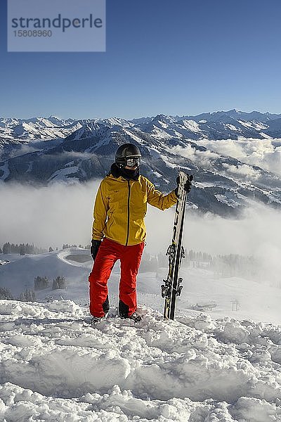 Skifahrer an der Skipiste stehend mit Ski in der Hand  Blick in die Ferne  Gipfel Hohe Salve  SkiWelt Wilder Kaiser Brixenthal  Hochbrixen  Tirol  Österreich  Europa
