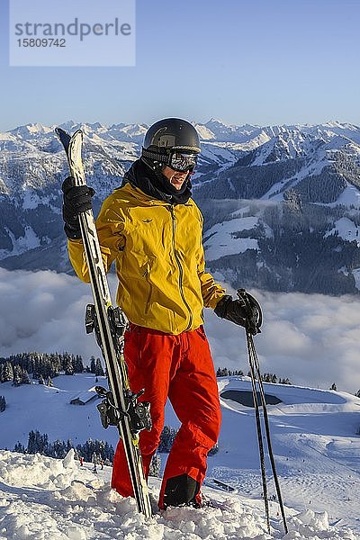 Skifahrer steht an der Skipiste und hält Ski  vor Bergpanorama  Gipfel Hohe Salve  SkiWelt Wilder Kaiser Brixenthal  Hochbrixen  Tirol  Österreich  Europa