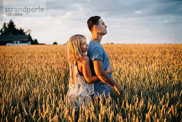Lächelndes junges Paar steht im goldenen Weizenfeld und umarmt sich.