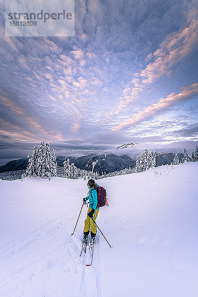 Person beim Skifahren durch eine winterliche Landschaft  Berge in der Ferne  dramatischer Himmel.