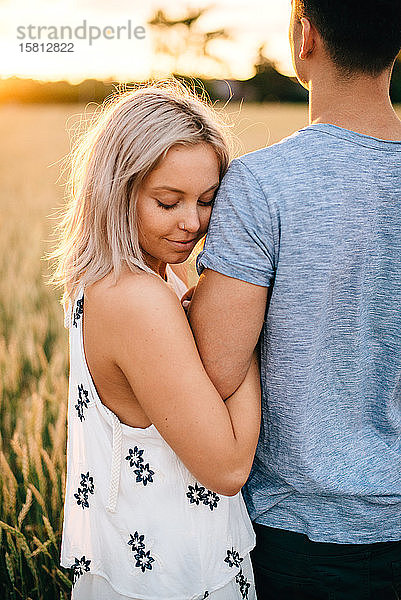 Lächelndes junges Paar steht im goldenen Weizenfeld und umarmt sich.