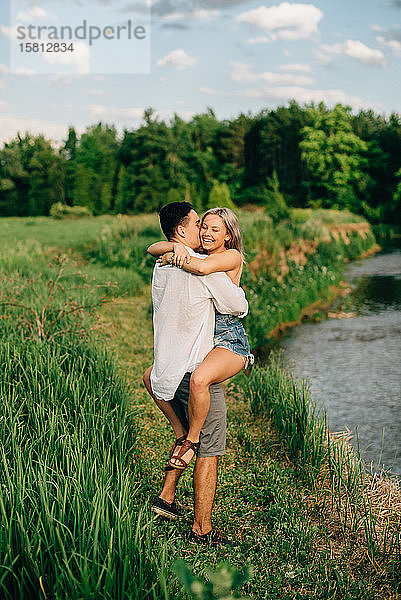 Junges Paar steht auf einem Weg an einem Fluss  umarmt und küsst sich.