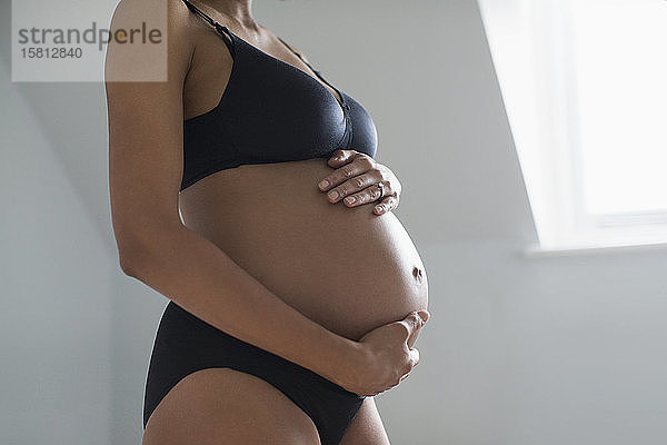 Schwangere Frau in BH und Höschen hält Bauch