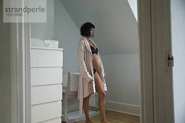 Gelassene schwangere Frau im Bademantel im Babyzimmer stehend