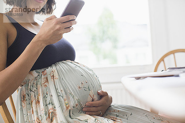 Schwangere Frau in geblümtem Kleid mit Smartphone