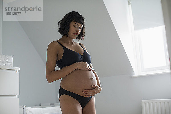 Serene schwangere Frau in BH und Höschen hält Bauch