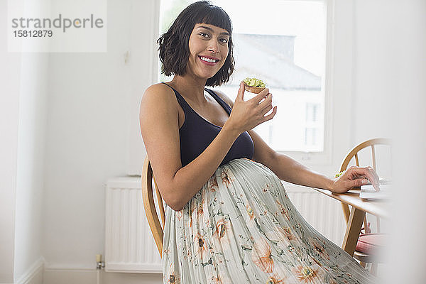 Porträt einer glücklichen schwangeren Frau  die Avocado-Toast isst