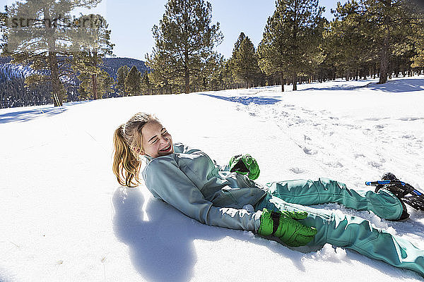 Ein Teenager-Mädchen mit Schneeschuhen liegt lachend im Schnee