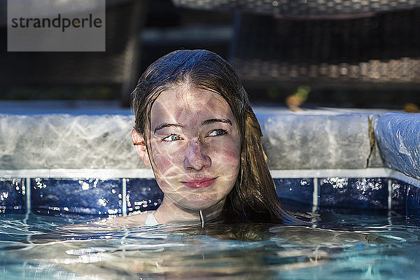 Ein dreizehnjähriges Teenagermädchen in einem Schwimmbad mit reflektiertem Licht  das auf ihrem Gesicht spielt