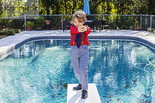 Ein sechsjähriger Junge steht auf einem Sprungbrett mit Blick auf den Pool