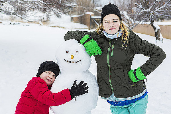 Bruder und Schwester  ein Junge und ein junges Mädchen lehnen sich im Winter an einen Schneemann