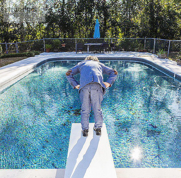 Ein sechsjähriger Junge steht auf einem Sprungbrett mit Blick auf den Pool