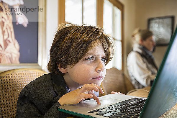 Ein sechsjähriger Junge  der zu Hause auf einem Laptop mit dem Cursor-Touchpad tippt.