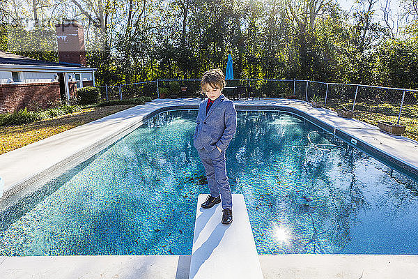 Ein sechsjähriger Junge steht auf einem Sprungbrett mit Blick auf den Pool
