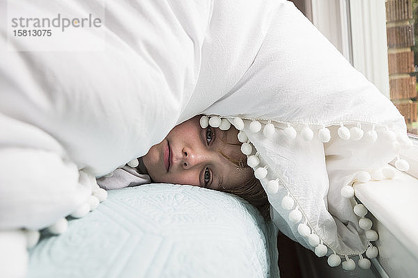 Ein sechsjähriger Junge im Bett mit Decken über dem Kopf