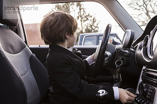 Ein sechsjähriger Junge sitzt im Auto und hält ein Lenkrad