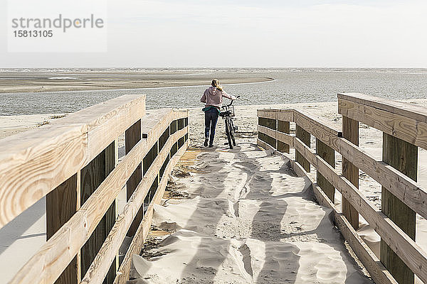 Teenagerin auf dem Fahrrad über die Brücke zum Strand