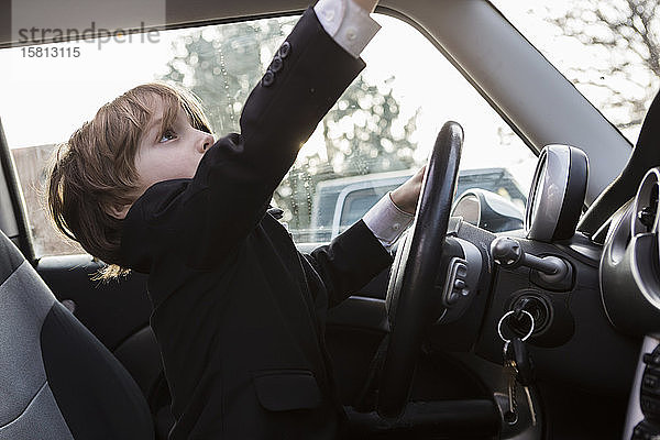 Ein sechsjähriger Junge sitzt im Auto und hält ein Lenkrad