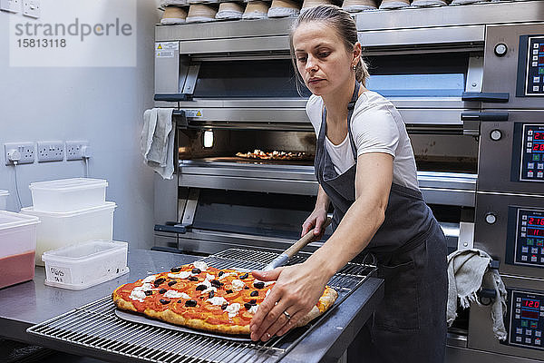 Frau mit Schürze steht in einer handwerklichen Bäckerei und bereitet Pizza für den Ofen vor.