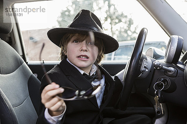 Ein sechsjähriger Junge sitzt im Auto und hält ein Lenkrad