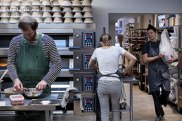 Zwei Frauen und ein Mann mit Schürzen  die in einer handwerklichen Bäckerei arbeiten.