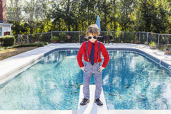 Ein sechsjähriger Junge steht auf einem Sprungbrett mit Blick auf den Pool