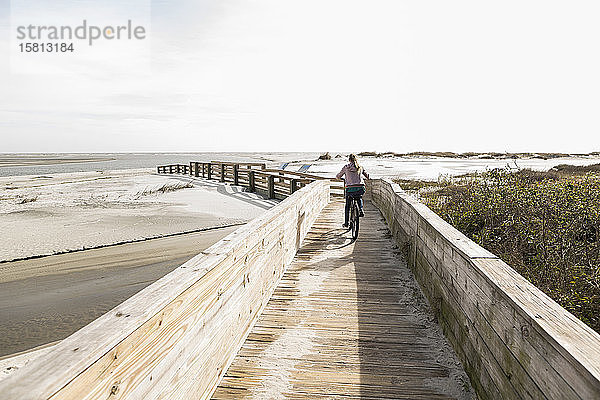 Teenagerin auf dem Fahrrad über die Brücke zum Strand
