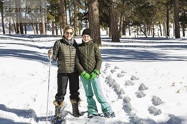 Eine erwachsene Frau und ein Teenager-Mädchen in Schneeschuhen im Wald mit Skistöcken