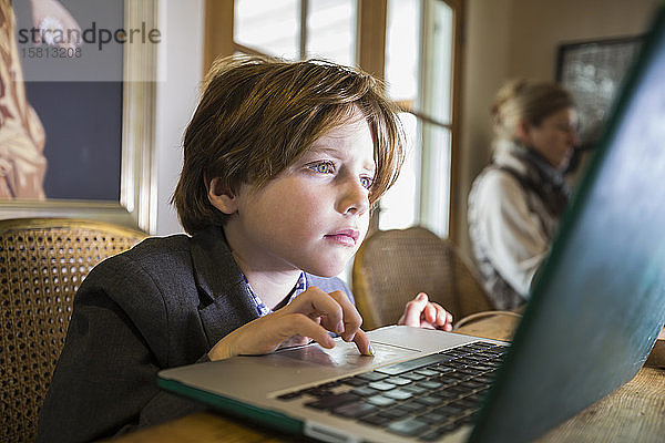 Ein sechsjähriger Junge tippt zu Hause auf einem Laptop