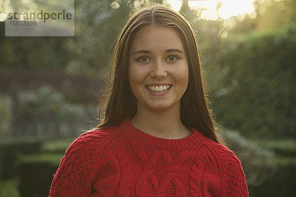 Porträt glückliches jugendliches Mädchen in rotem Pullover im Park