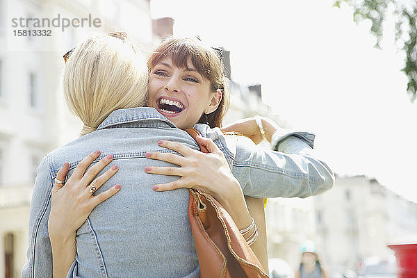 Glückliche junge Frauen  die sich auf einem sonnigen Bürgersteig umarmen