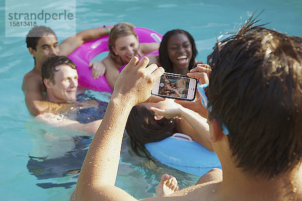 Jugendlicher mit Fotohandy fotografiert Freunde im Schwimmbad
