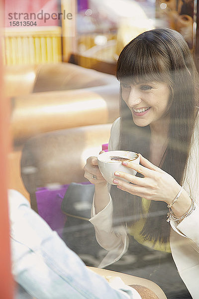 Glückliche junge Frau genießt einen Cappuccino im Caféfenster